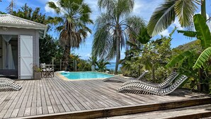Une terrasse en bois avec une piscine, des chaises longues et un petit pavillon.