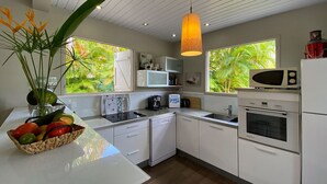 Une cuisine moderne avec des meubles blancs, un four à micro-ondes encastré, une machine à café et un panier de fruits posé sur le plan de travail.