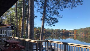 A wooden deck with a picnic table, overlooking a calm lake with trees in the background.