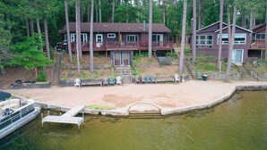 A lakeside cabin with a dock, a sandy beach, and a forested backdrop.