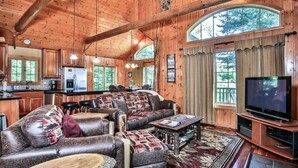 A cabin interior with a living room, kitchen, and a large window. - Lakefront log cabin on Lost Lake with dock, kayaks, large deck, and fire pit! (St. Germain)
