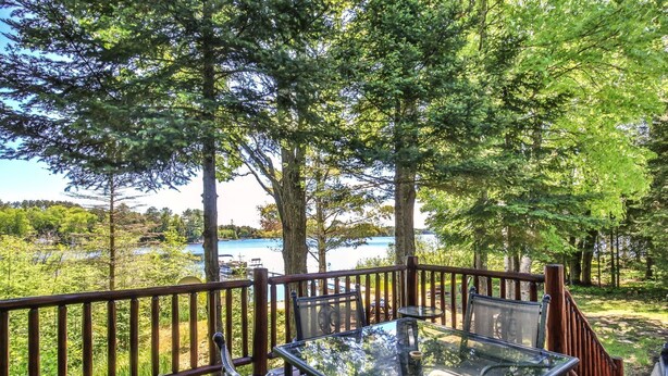 A glass-top table with chairs on a wooden deck overlooking a lake. - Lakefront log cabin on Lost Lake with dock, kayaks, large deck, and fire pit! (St. Germain)