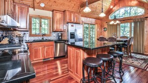 A spacious kitchen with wooden cabinets, a stainless steel refrigerator, and a bar area with stools. - Lakefront log cabin on Lost Lake with dock, kayaks, large deck, and fire pit! (St. Germain)