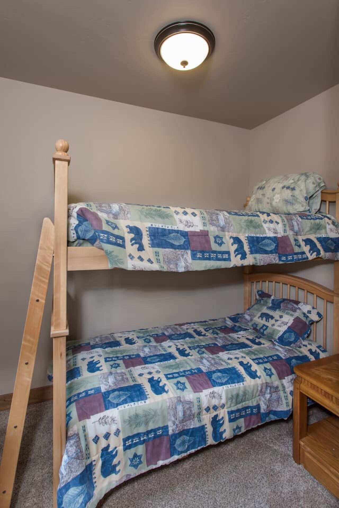 Una cama litera con cubrecama acolchado, una escalera de madera y una pequeña mesa de madera.