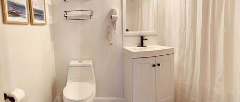 A bathroom with a toilet, sink, and mirror. There are framed pictures on the wall and a shower curtain.