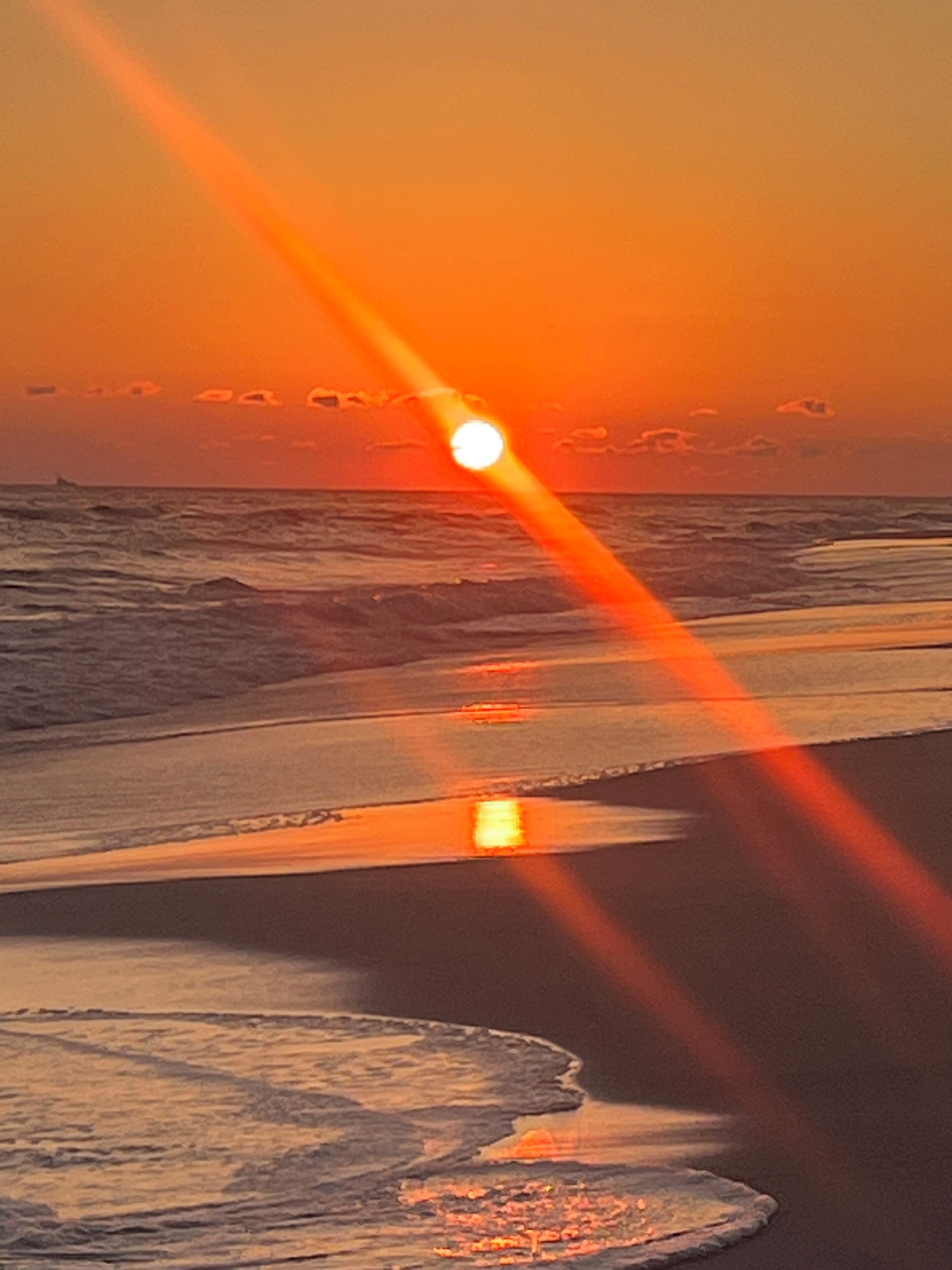 Un coucher de soleil sur une plage, avec des vagues et un ciel dégagé.