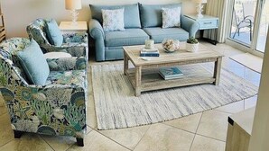 Un salon comprenant un canapé, un fauteuil et une table basse, agrémenté d’un tapis sur le thème de la plage et de décorations en forme d’étoiles de mer.