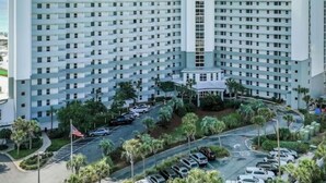 Un grand hôtel à plusieurs étages, doté d’une tour centrale, d’un parking et d’un espace vert environnant.