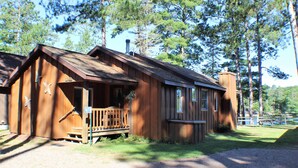 Une cabane en bois dotée d’un porche et d’une cheminée, entourée d’arbres.