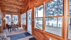 Une cabane en bois dotée de grandes fenêtres, d’un coin repas et offrant une vue sur un lac.