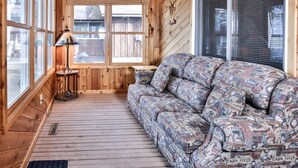 L’intérieur d’un chalet accueillant, avec un plancher en bois, un canapé à motifs, une lampe et de grandes fenêtres.