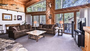 Un intérieur de chalet chaleureux avec un plafond en bois, de grandes fenêtres, une cheminée et un mur d’accent en pierre.