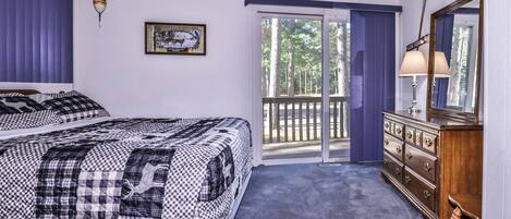 Un dormitorio con una cama grande, un aparador, un espejo y una ventana con vistas a árboles.
