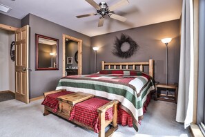 A bedroom with a wooden bed, a ceiling fan, a mirror, a wall-mounted wreath, and a bedside lamp.