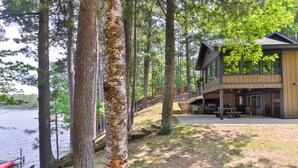 Uma cabana com varanda com vista para um lago, rodeada por árvores altas.