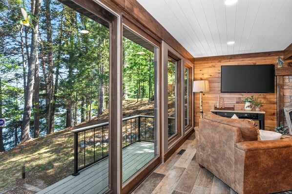 A modern living room with large windows, a wooden interior, and a flat-screen TV.