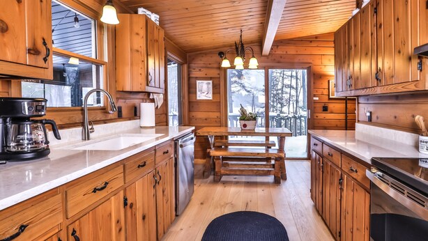 A wooden cabin kitchen with a central island, wooden cabinets, a coffee maker, and a view of the outdoors. - Large lakeside 'treehouse' with enclosed porch, dock, pool table, and fire pit! (St.Germain)