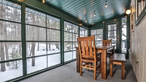 A cozy room with a large window, a wooden table, and chairs. - Large lakeside 'treehouse' with enclosed porch, dock, pool table, and fire pit! (St.Germain)