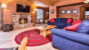 A cozy cabin interior with a brick fireplace, a blue sofa, and a wooden ceiling. - Large lakeside 'treehouse' with enclosed porch, dock, pool table, and fire pit! (St.Germain)
