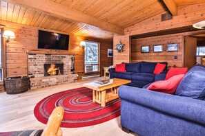 A cozy cabin interior with a brick fireplace, a blue sofa, and a wooden ceiling.