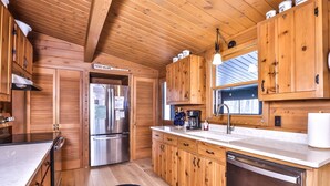 A wooden cabin-style kitchen with a stainless steel refrigerator, wooden cabinets, a coffee maker, and a dishwasher. - Large lakeside 'treehouse' with enclosed porch, dock, pool table, and fire pit! (St.Germain)