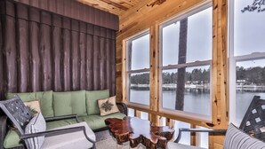 A cozy cabin interior with a green sofa, a wooden coffee table, and a view of a lake through large windows.
