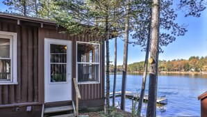 A cabin with a dock extending into a lake, surrounded by trees and a clear sky.