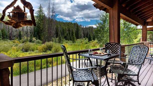 A wooden deck with metal chairs and a table, overlooking a forested area.