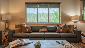 A living room with a sofa, a coffee table, and a large window with a forest view.