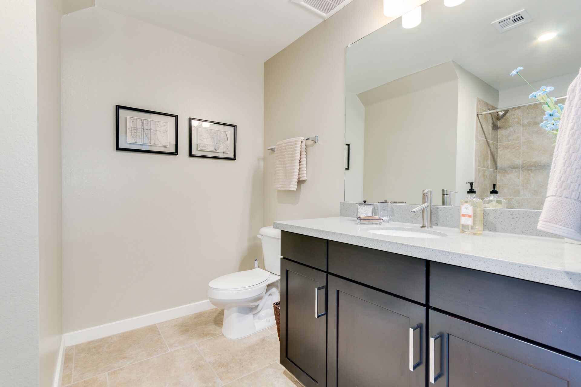 Une salle de bain moderne avec des toilettes, un lavabo et un miroir. Des tableaux encadrés ornent le mur et une serviette est accrochée sur le côté.