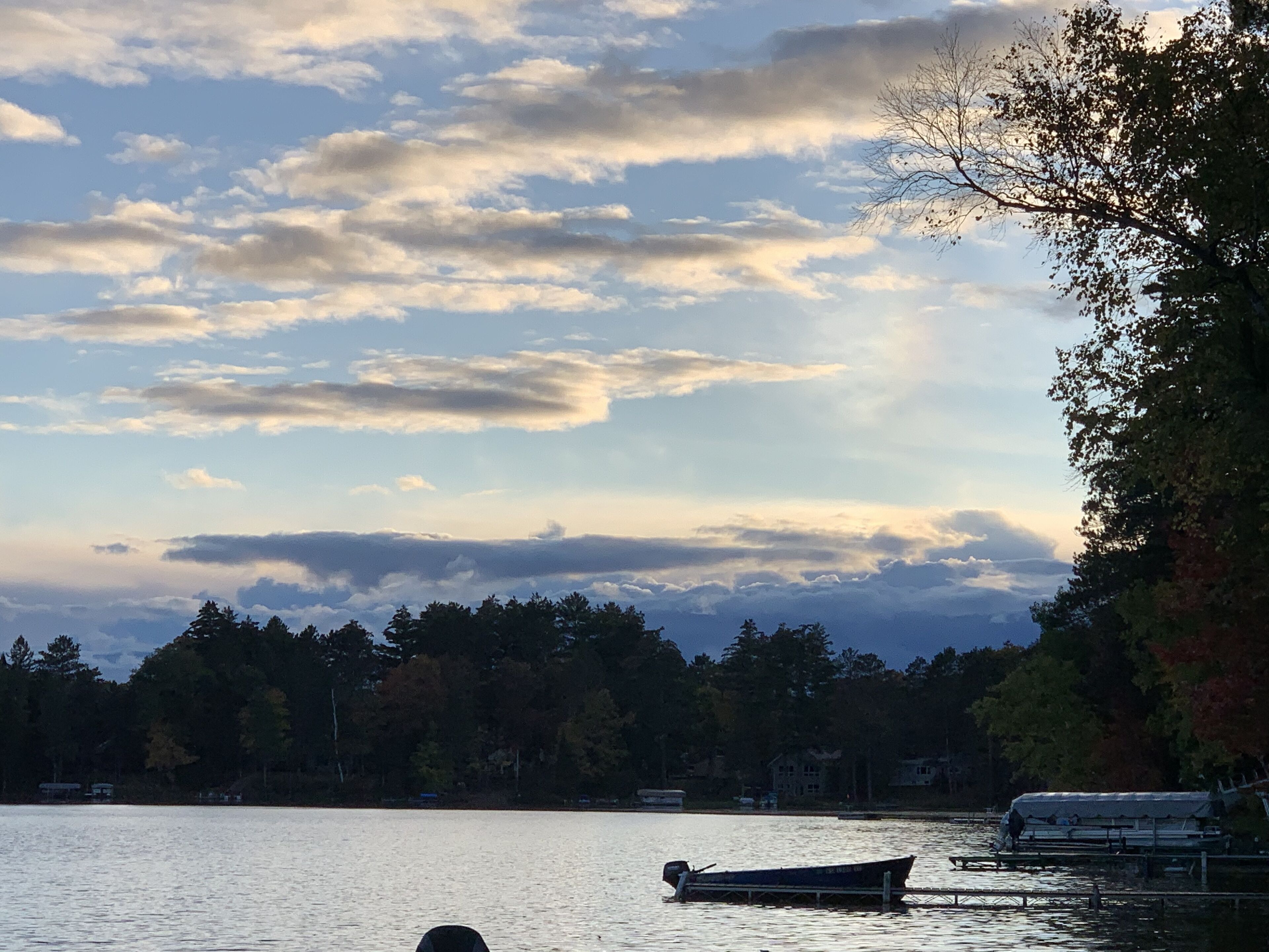 Un lago con un bote amarrado a la derecha, rodeado de árboles y un cielo nublado.