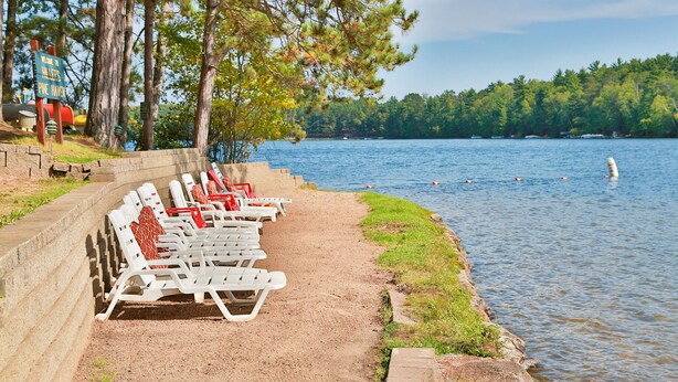 Zona junto al lago con sillones blancos y un cartel de bienvenida a Pine Haven.