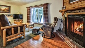 Un salón acogedor con chimenea, un sofá de cuero, una mesa de centro de madera y un televisor.