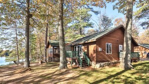 A cabin with a porch and a staircase leading to a deck, surrounded by trees and a lake.