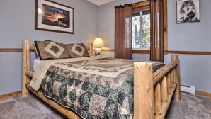 A wooden bed with a quilt, a nightstand with a lamp, and a window with curtains.