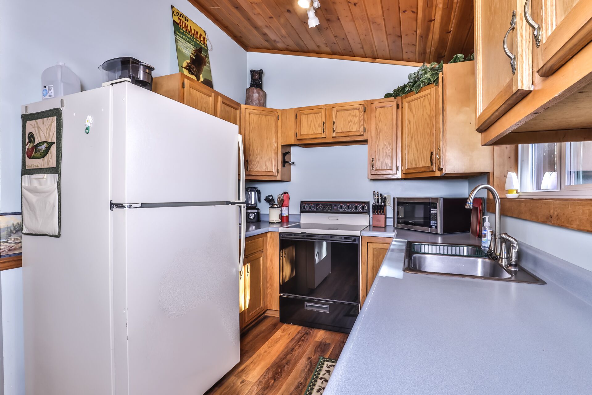 A modern kitchen with wooden cabinets, a white refrigerator, a stove, a microwave, and a sink.