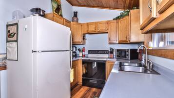 A modern kitchen with wooden cabinets, a white refrigerator, a stove, a microwave, and a sink.