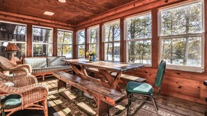 A wooden cabin interior with a large dining table, wicker chairs, and a bench.