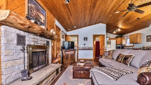 A cozy living room with a stone fireplace, wooden ceiling, and a sofa with patterned cushions.