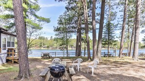 A campsite with a grill, picnic tables, and a cabin by a lake.