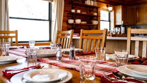 Una mesa de madera para comer con platos, vasos y cubiertos, adornada con un mantel a cuadros.