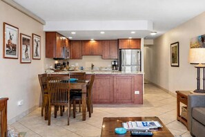 A modern kitchen with wooden cabinets, stainless steel appliances, and a dining area with a table and chairs. - Kamaole Sands 9-301 - Luxurious Renovation, Split AC, Wi-Fi, Ocean View Condo (Kihei)