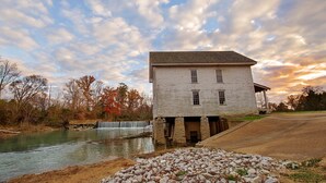 Un bâtiment historique en pierre blanche, avec des fondations en pierre, une petite cascade et une rivière au premier plan.