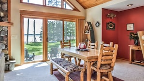 A dining area with a wooden table and chairs, a bench, and a view of a lake through large sliding glass doors.