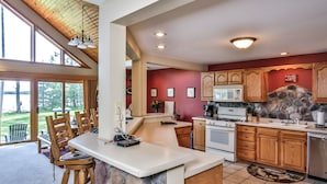 A spacious kitchen with a stone island, wooden cabinets, and a large window overlooking a scenic outdoor area.