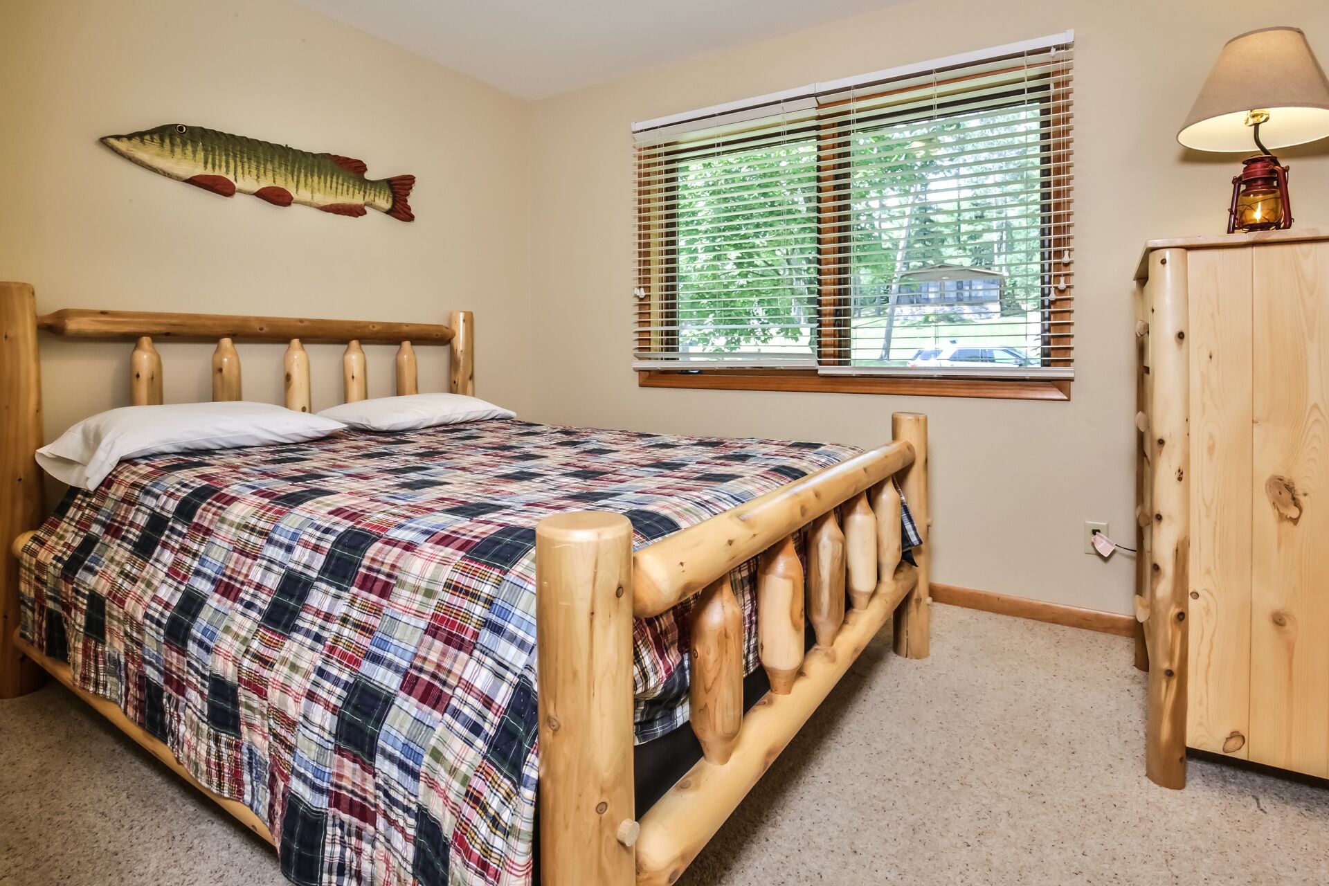 Un dormitorio con cama de madera, colcha escocesa, decoración de pez, ventana con persianas y mesita de noche de madera.