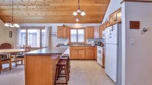 Une cuisine avec des meubles de rangement en bois, un îlot central doté de tabourets, un réfrigérateur et un coin repas avec des chaises et une table.