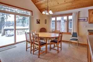 A cozy dining area with a wooden table and chairs, large windows with curtains, and a view of a snowy outdoor deck. - Elbert’s Resort lakeside cabin with dock and Timber’s bar and grill on site! (St.Germain)