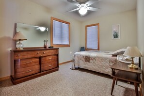 A bedroom with a wooden dresser, a bed with a quilt, a ceiling fan, and two windows with blinds. - Elbert’s Resort lakeside cabin with dock and Timber’s bar and grill on site! (St.Germain)
