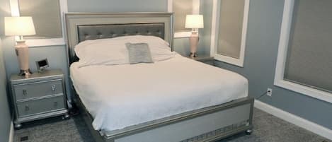 Un dormitorio con una cama grande, dos mesitas de noche con lámparas y una ventana con persianas.